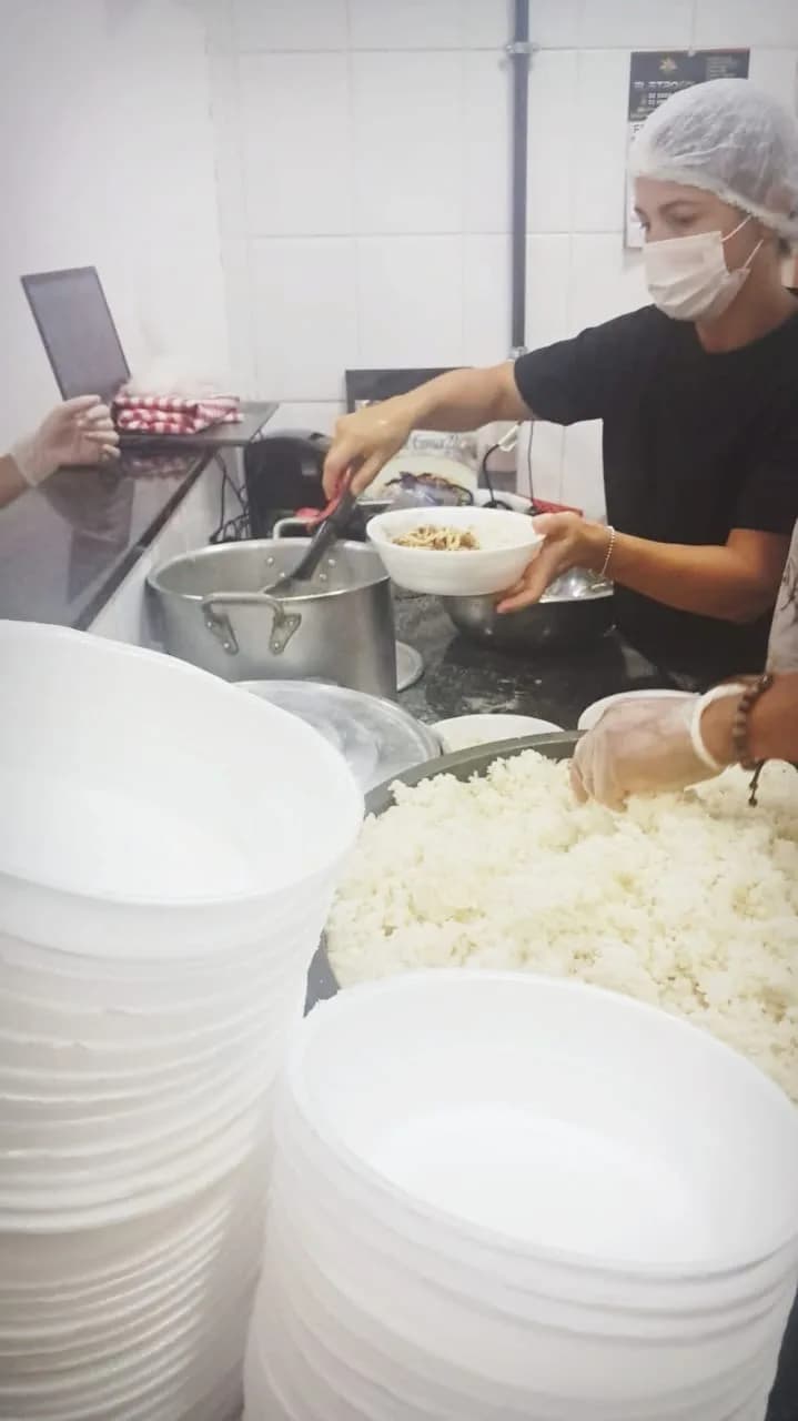 Voluntário servindo arroz e prato quente nas marmitas