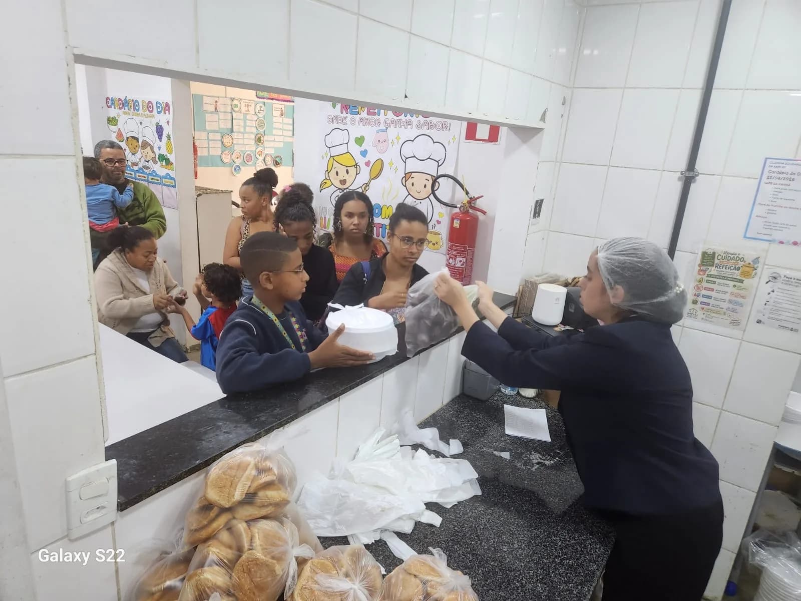 Equipe entregando marmitas, pães e bananas às famílias na janela da Cozinha Solidária