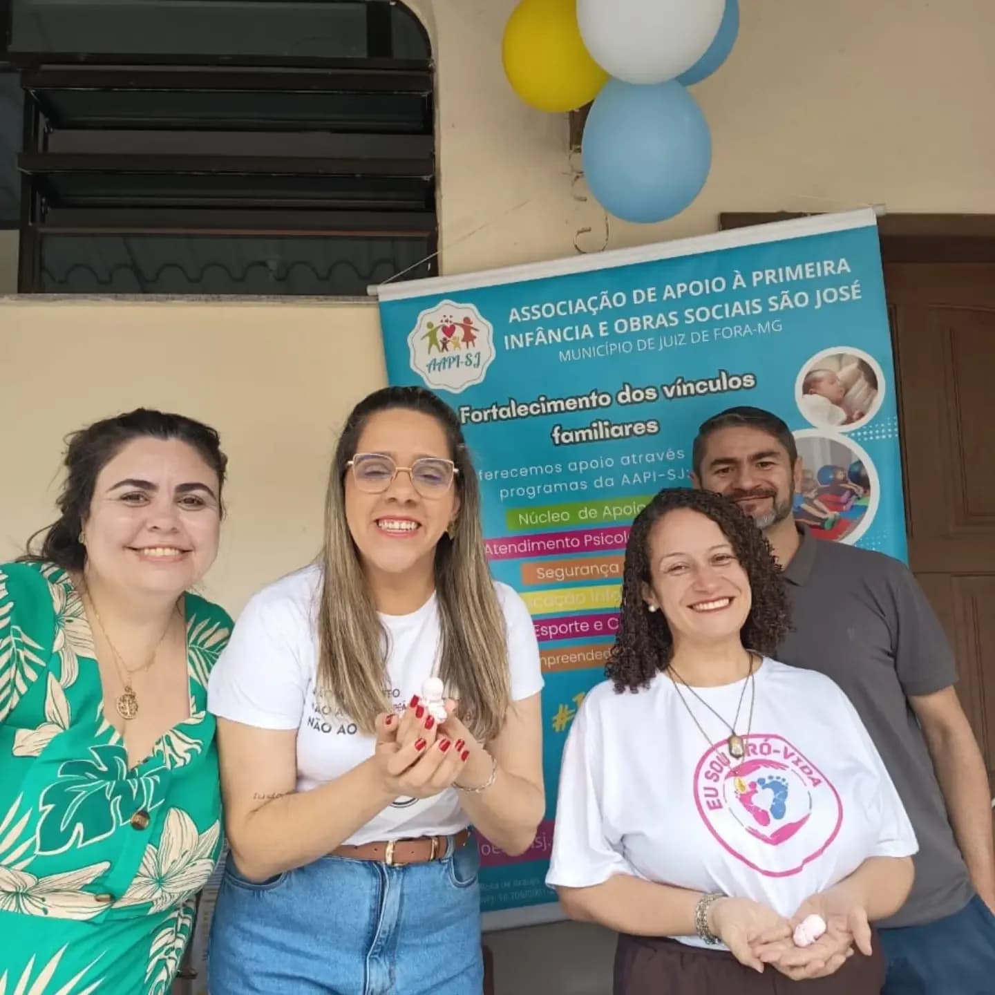 Voluntárias da AAPI-SJ diante do banner da associação