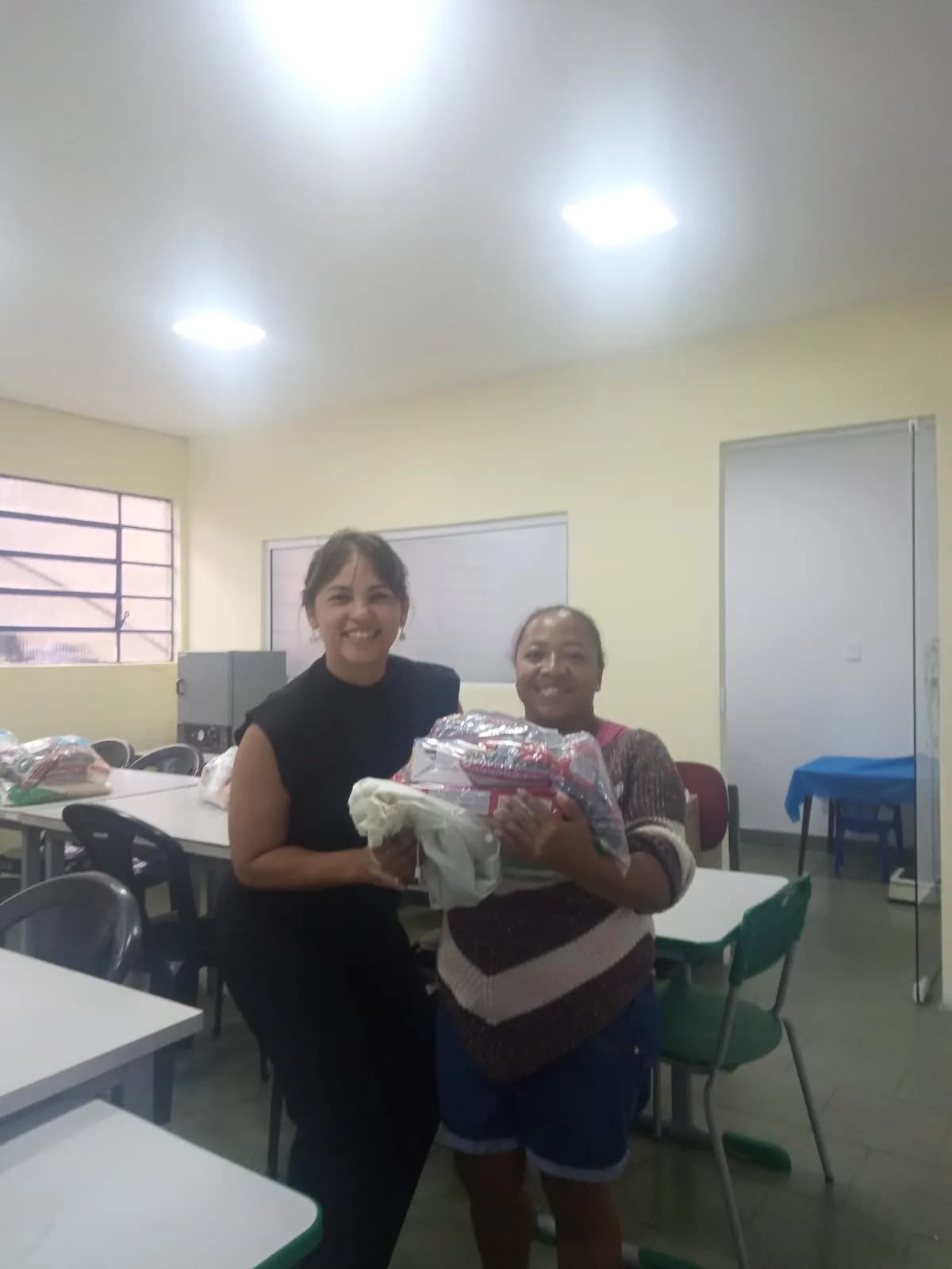 Equipe e mãe assistida sorrindo com a cesta básica recebida