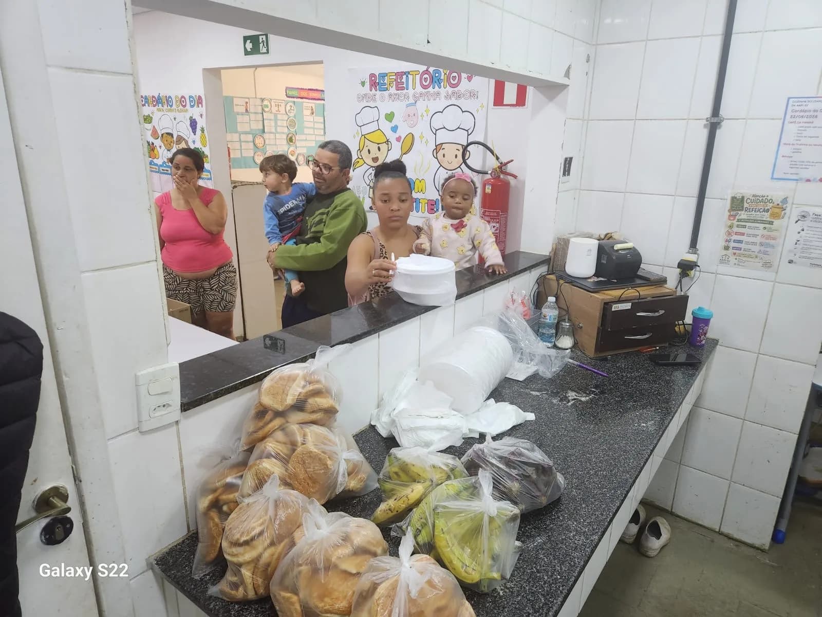 Famílias na fila da janela da Cozinha Solidária recebendo as marmitas