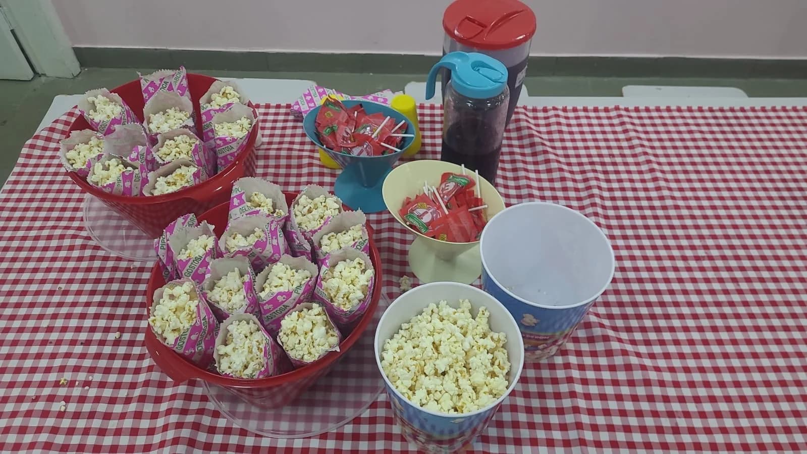 Mesa com pipoca, pirulitos e suco na festa