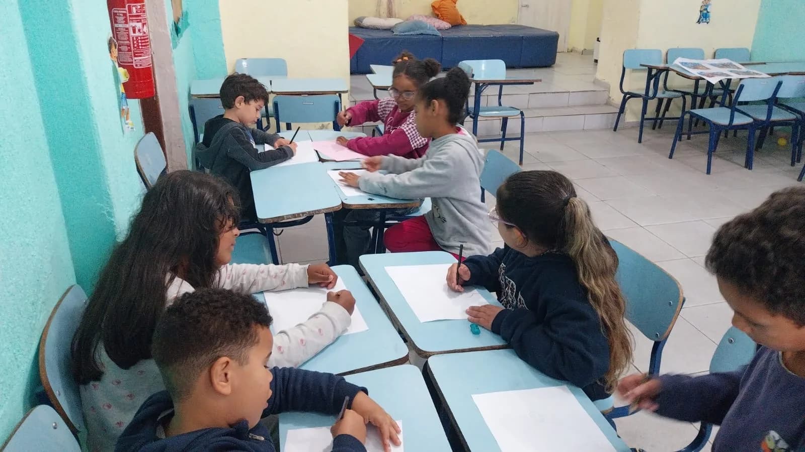 Crianças reunidas em grupos desenhando na sala de atividades