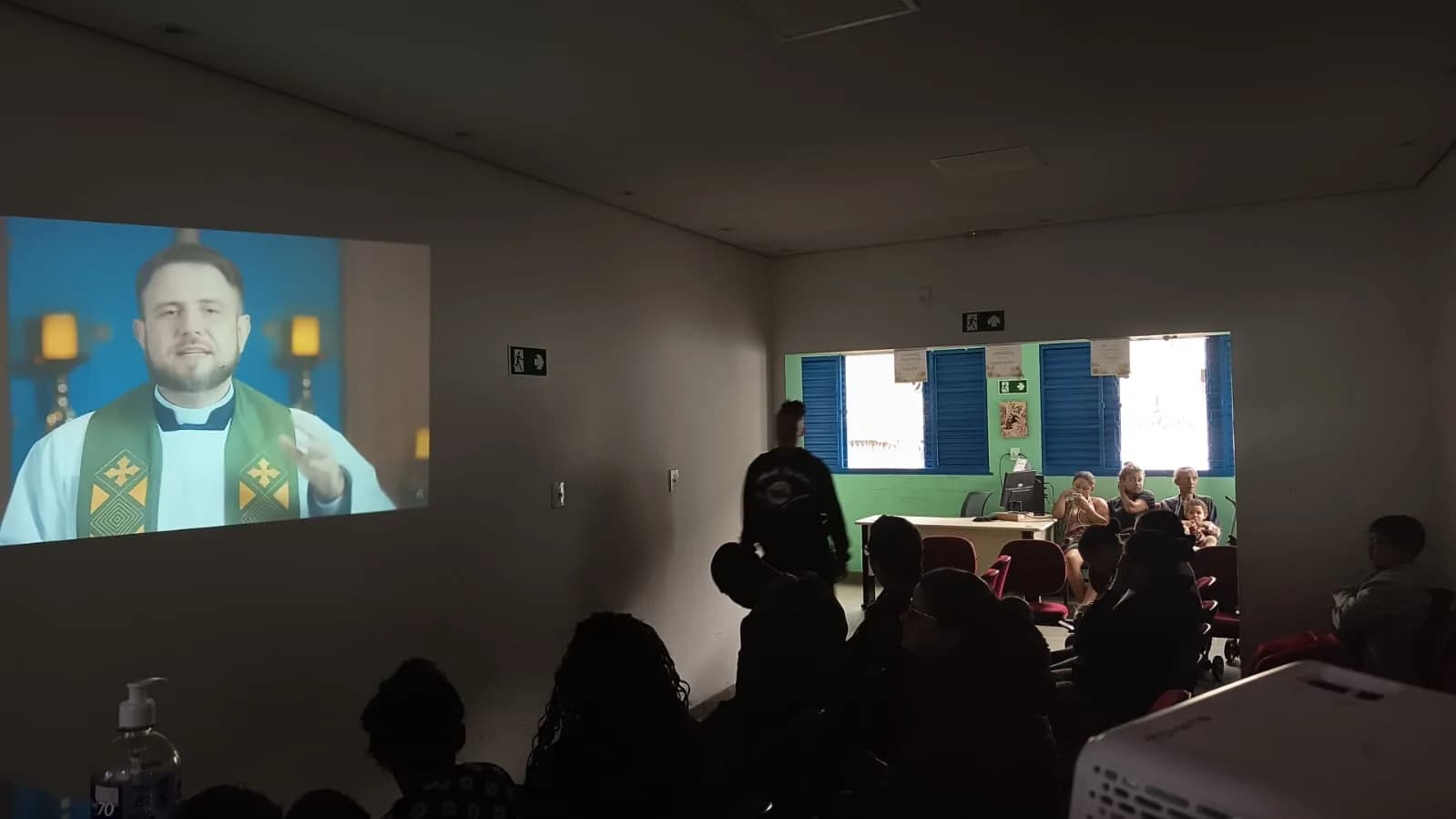 Famílias acompanhando a mensagem de um padre por vídeo no encontro de sábado