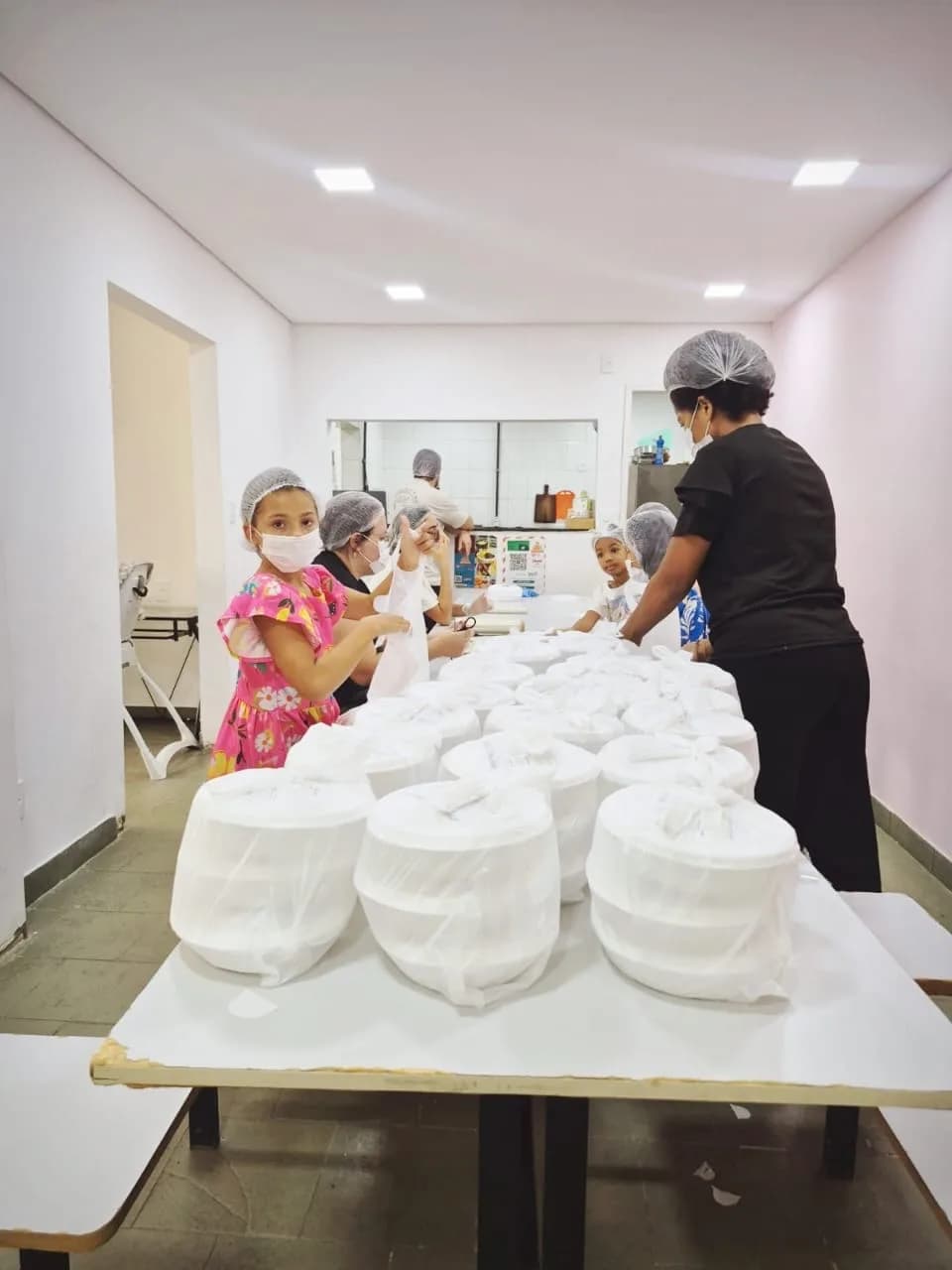 Voluntários e crianças ajudando a embalar as marmitas
