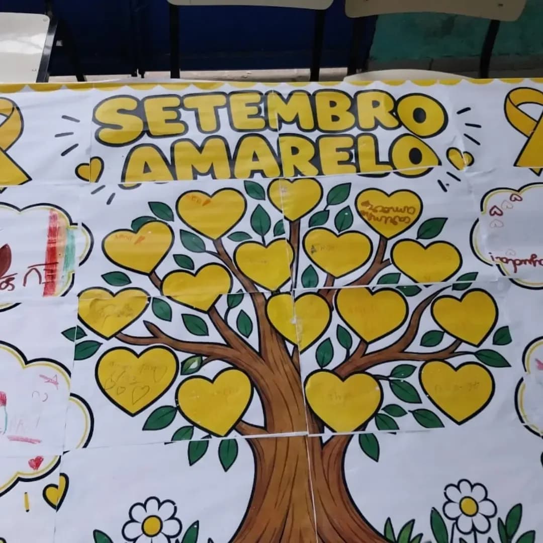 Painel do Setembro Amarelo feito pelas crianças: uma árvore com corações amarelos escritos à mão.