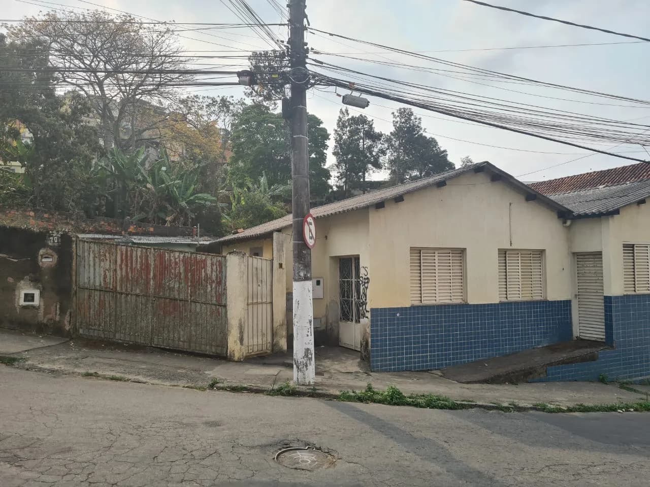 Fachada da estrutura antiga da sede, casa simples com azulejos azuis e portão enferrujado, em Granjas Betânia