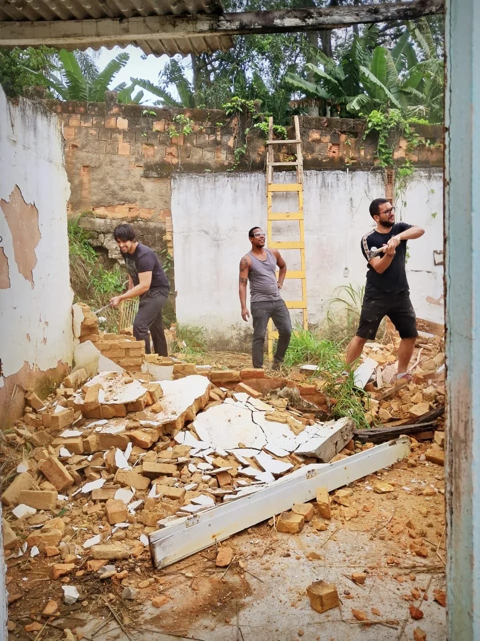 Três voluntários demolindo muro no quintal