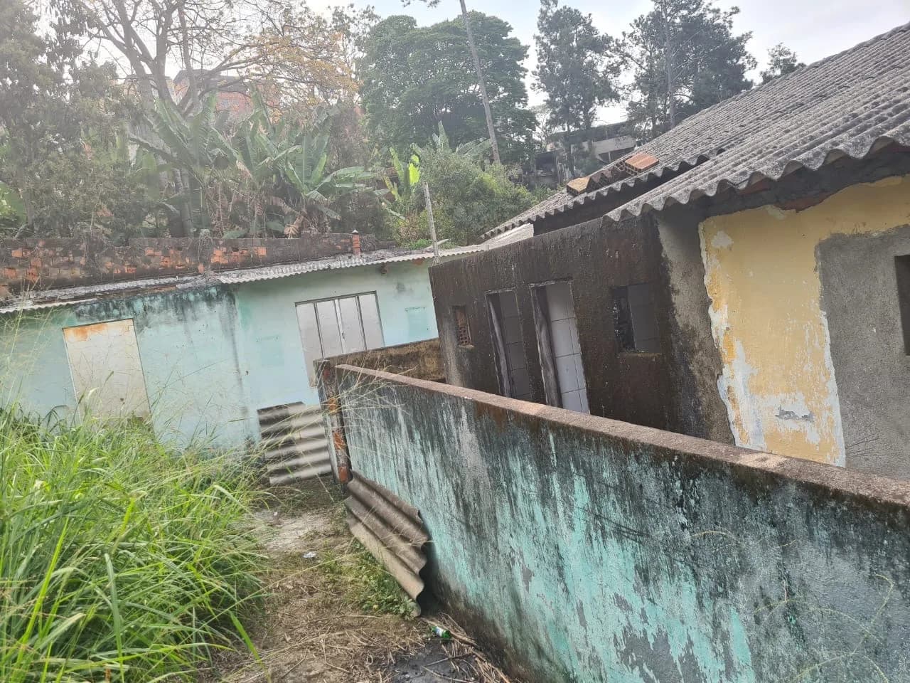 Quintal da estrutura antiga da sede, com mato alto e construções deterioradas, em Granjas Betânia