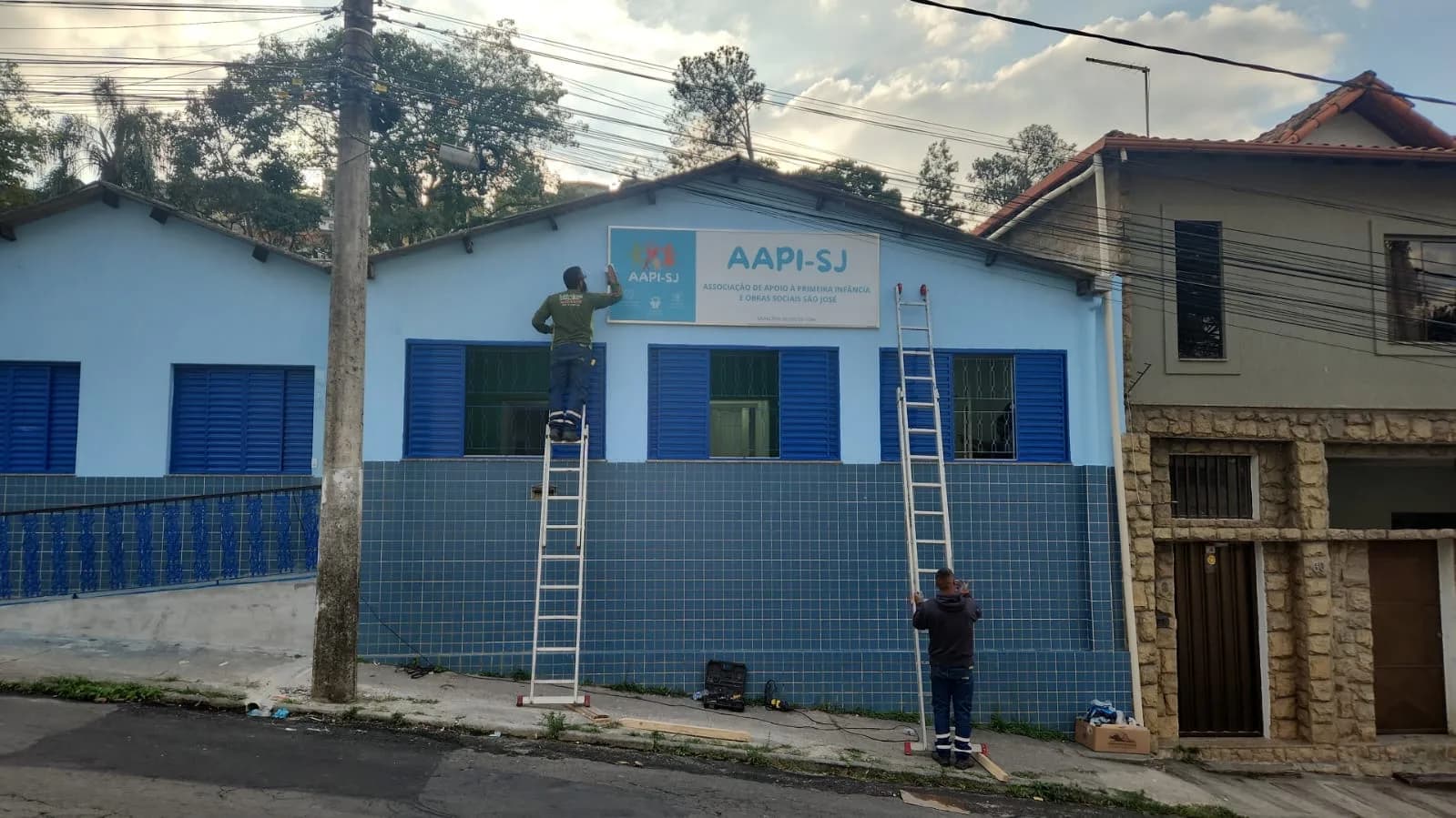 Fachada pintada de azul, com a placa da AAPI-SJ sendo instalada